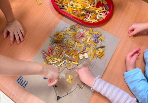 Dzieci wyklejają obrazek jeża makaronem