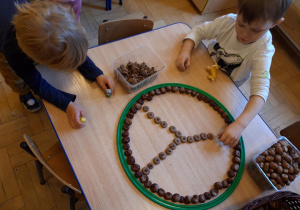 Dzieci wykonują mandalę z żołędzi.